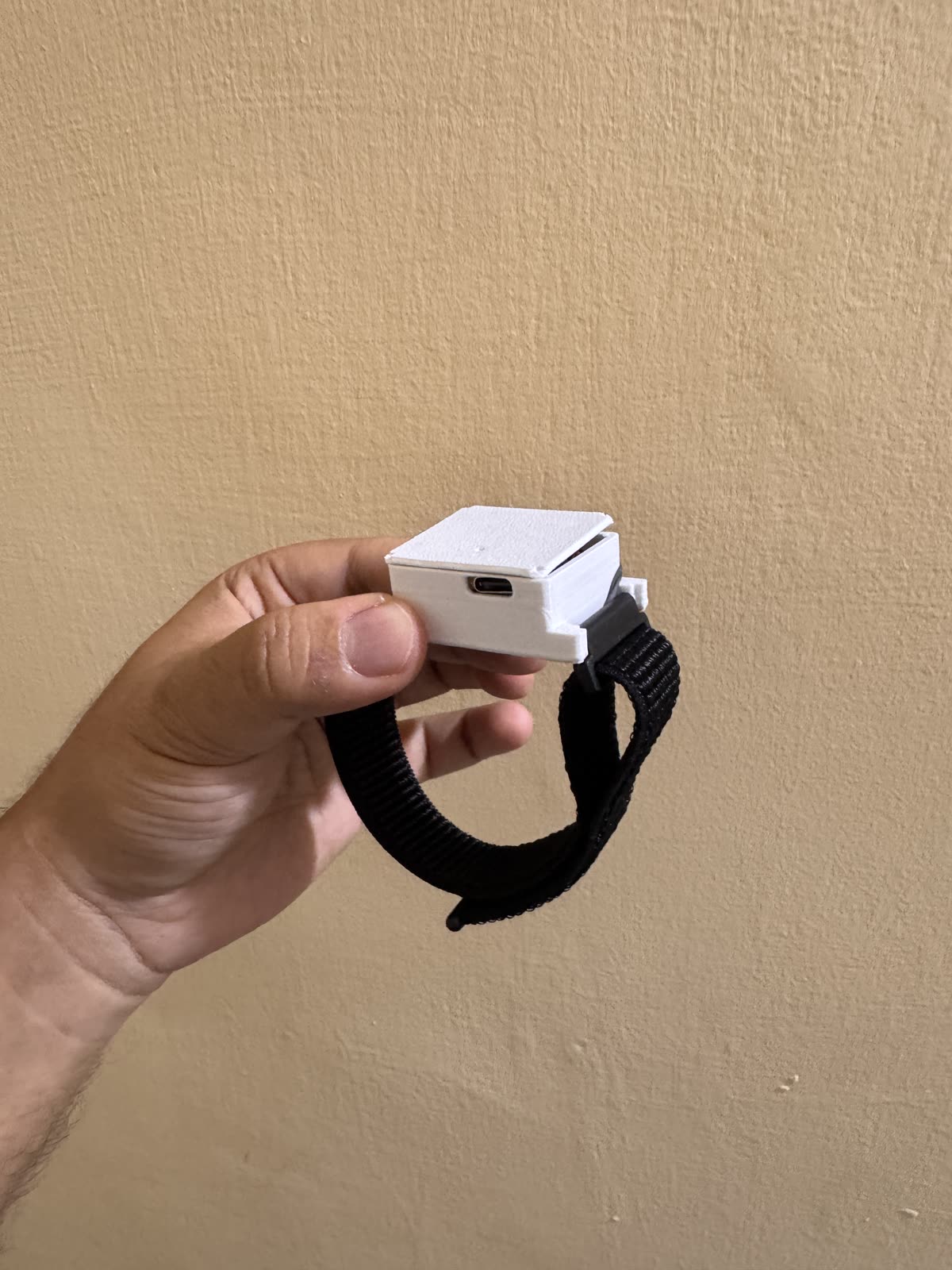 Keepshake prototype held in hand, showing its white enclosure, USB-C port, and black woven strap